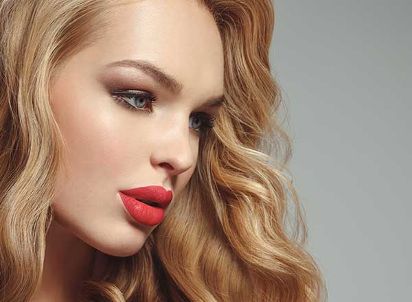 Close-up of a woman with flawless skin and bold red lips, highlighting the cosmetic enhancement results achievable with injectables at Revive Aesthetics Med Spa.